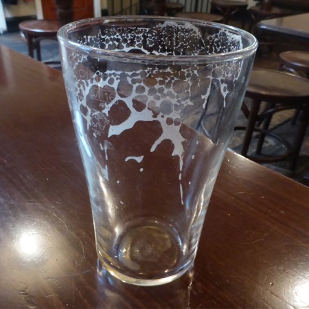 An empty pint glass on a table in a pub.